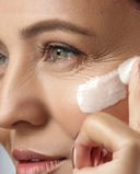 Close-up of a woman applying white cream to her cheek with her finger.