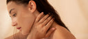 Woman with hand on neck against a beige background