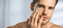 Man applying cream to his face with a neutral background