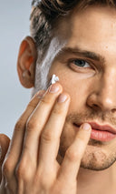Man applying cream to his face with a neutral background