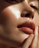 Extreme close-up of a woman's face with warm directional sunlight highlighting her cheek, nose, lips, and fingers. 