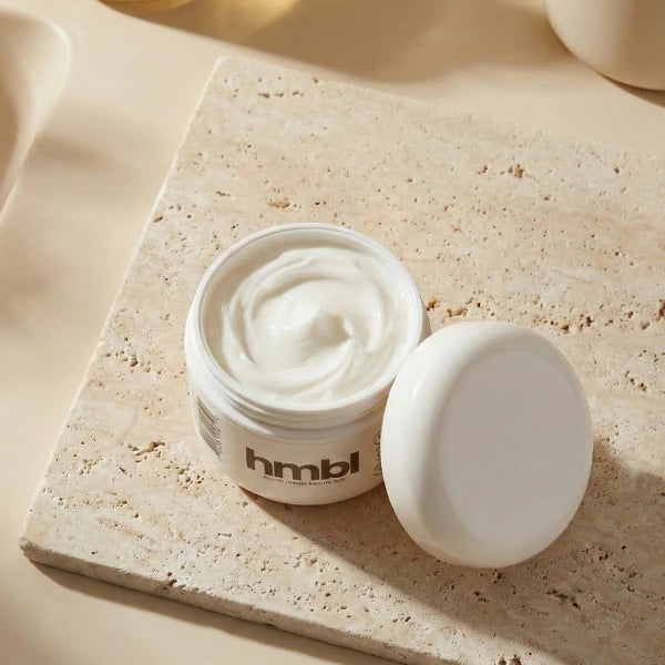 Open jar of hmbl rich cream moisturizer on a beige stone surface