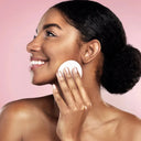 Woman applying cream to her face with a pink background