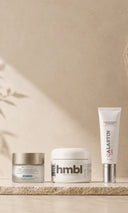 Three skincare products arranged on a textured beige surface against a warm beige wall: Skinceuticals Triple Lipid Moisturizer, hmbl Rich Moisturizing Cream, Alastin Ultra Nourishing Moisturizer